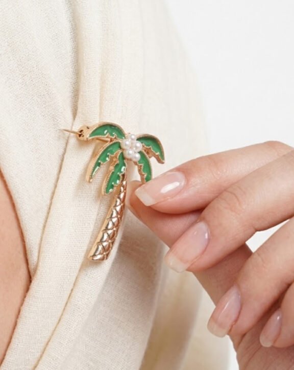 This Palm Tree Pearl Brooch Pin features green enamel palm leaves with a faux pearl coconut cluster, adding a fun tropical touch to your hijab or scarf. Features: Gold tone finish Green enamel palm leaves Faux pearl cluster detail Secure pin backing Why You Should Buy: A playful, tropical-inspired design that adds personality to everyday hijab or scarf styling. Perfect For: Casual styling Summer looks Gifting